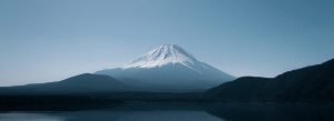 Snow-capped Mount Fuji reflected over a calm lake with surrounding mountains in Japan