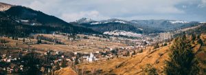 Panoramic view of a traditional village in Bucovina with rolling hills and the Carpathian Mountains in the background