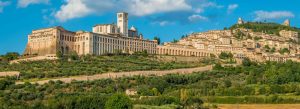 Panoramic view of Assisi featuring the hilltop town and the Basilica of Saint Francis of Assisi surrounded by lush green countryside.