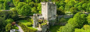 Blarney Castle in County Cork surrounded by green gardens and trees under bright daylight