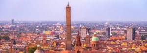 Panoramic skyline of Bologna at sunset featuring the historic Asinelli Tower rising above colorful rooftops
