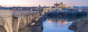 Evening view of the Roman Bridge of Córdoba over the Guadalquivir River with the illuminated Mosque–Cathedral of Córdoba in the background