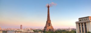 Sunset view of the Eiffel Tower rising above the Paris skyline with warm evening light.