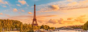 Golden sunset view of the Eiffel Tower along the Seine River with a bridge and tree-lined banks in Paris