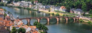 Panoramic view of Old Bridge Heidelberg spanning the Neckar River with historic rooftops and riverside buildings in Heidelberg.