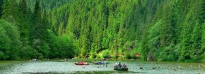 People rowing boats on Red Lake surrounded by dense pine forests in the Carpathian Mountains