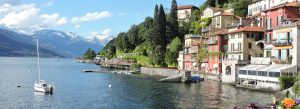 Colorful lakeside village on Lake Como with alpine mountains and a sailboat in northern Italy