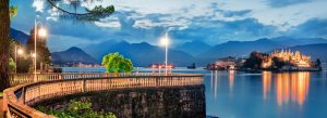 Evening view of Lake Maggiore with illuminated Isola Bella and scenic promenade overlooking calm water and mountains