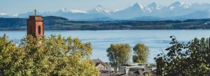 Scenic view of Lake Zurich with a church tower in the foreground and snow-capped Swiss Alps in the background