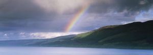 Rainbow over scenic lake and green hills in the Scottish Highlands under dramatic cloudy sky