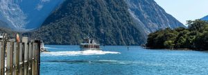 Cruise boat sailing through Milford Sound surrounded by steep forested mountains and clear blue water New Zealand
