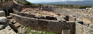 Ancient circular stone grave circle at Mycenae archaeological site in Greece with visitors and surrounding hills