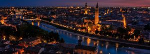 Night view of Verona with illuminated skyline along the Adige River and historic bridges reflecting city lights
