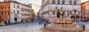 Historic medieval square in Perugia featuring the iconic Fontana Maggiore and surrounding Gothic architecture at sunset