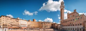 Panoramic view of Piazza del Campo with the Palazzo Pubblico and Torre del Mangia under a bright blue sky