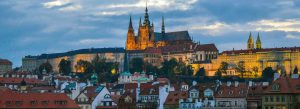 Panoramic view of Prague Castle and St. Vitus Cathedral overlooking red-roofed Old Town buildings in Prague at sunset.