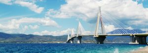 Cable-stayed bridge stretching over blue sea with mountains in the background under a bright sky