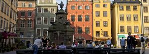 Colorful historic buildings and central fountain in a lively European old town square with people relaxing and walking