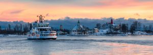 Passenger ferry cruising past a snowy island village at sunset with colorful sky in a Nordic coastal city