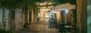 Charming cobblestone alley with outdoor café seating in Rome illuminated at night with ivy-covered walls