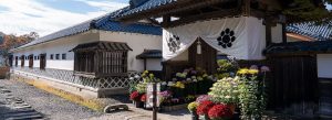 Traditional samurai residence entrance with white walls and flowers at Aizu Bukeyashiki in Aizuwakamatsu, Japan.