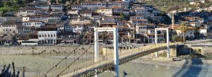 View of Berat City, Albania, featuring traditional Ottoman-style houses and the historic suspension bridge over the Osum River.