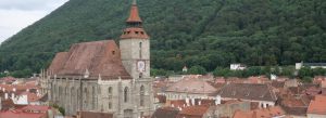 Historic Black Church in Brașov, Romania, with red rooftops and green mountains in the background.