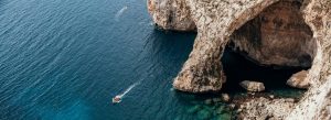 Boat entering the Blue Grotto sea cave with turquoise waters and limestone cliffs in Malta.