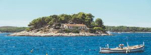 Boat floating near Lokrum Island with pine trees and stone house on the Adriatic coast in Croatia