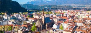Aerial view of Bolzano, Italy, surrounded by the Dolomite mountains with historic buildings and alpine scenery.