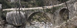 Historic stone Brataj Bridge crossing a rocky canyon in southern Albania surrounded by rugged mountain landscape.