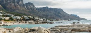 Camps Bay Beach in Cape Town with turquoise ocean, rocky shoreline and the Twelve Apostles mountains in the background.