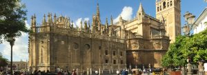Exterior view of the Cathedral of Seville in Spain featuring Gothic architecture and historic towers under a blue sky.