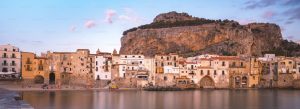 Colorful seaside houses of Cefalù with sandy beach and rocky cliff in Sicily, Italy at sunset