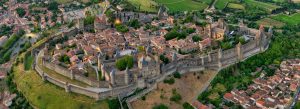 Aerial view of the fortified medieval citadel of Cité de Carcassonne in southern France, featuring ancient stone walls, towers, and historic buildings surrounded by lush countryside.