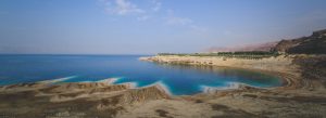Salt formations along the Dead Sea shoreline with turquoise water and desert landscape under a clear sky