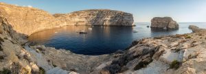 Panoramic view of Dwerja Bay in Gozo, Malta with rocky cliffs, turquoise waters, and sailing boats