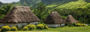 Traditional Fijian village with thatched bures surrounded by lush green hills and palm trees in Fiji