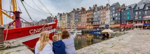 Colorful harbor in Honfleur, France with traditional fishing boats and historic waterfront buildings.