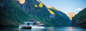 Modern cruise boat sailing through a dramatic Norwegian fjord surrounded by steep green mountains