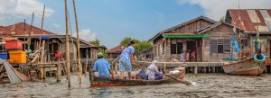 Local family traveling by wooden boat through traditional floating villages in Cambodia