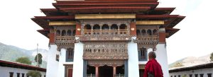 Gangteng Monastery in Bhutan with intricate Bhutanese architecture and a monk standing in the courtyard.
