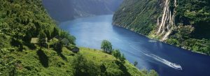Beautiful view of Geirangerfjord with waterfalls, green cliffs, and cruise boat in Norway.