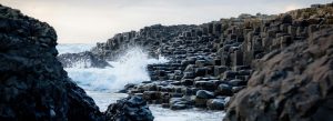 Basalt hexagonal stones at Giant’s Causeway on the Northern Ireland coast with waves crashing against the rocky shoreline.