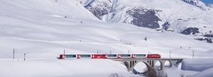 Red Glacier Express train crossing a stone bridge through the snowy Swiss Alps in Switzerland.