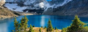 Turquoise alpine lake surrounded by snow-covered mountains and pine trees in Glacier National Park, Canada