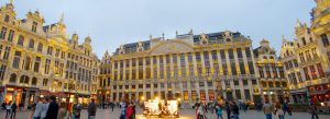 Grand Place in Brussels, Belgium, illuminated historic guild houses and Town Hall at dusk with tourists walking through the central square.