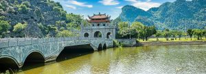 Ancient stone bridge leading to Hoa Lu Ancient Capital surrounded by limestone mountains and tranquil water in Ninh Binh, Vietnam