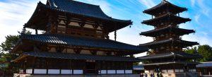 Ancient wooden buildings and five-story pagoda at Hōryū-ji Buddhist Temple in Japan under a bright blue sky.