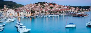 Scenic waterfront view of Hvar Island, Croatia, with luxury yachts, historic stone houses, and a picturesque Adriatic harbor at sunset.